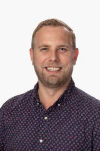 Dr. David Awde. He is posing for a full profile shot and is wearing a blue and red polka-dot shirt.