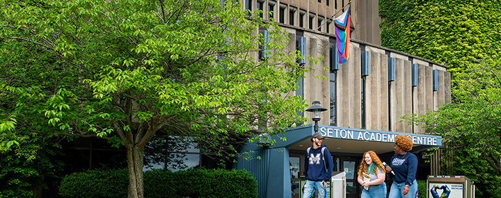 MSVU Students walking outside of Seton Academic Centre with the Pride flag on the flagpole