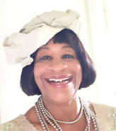 Mavis (Grosse) Akasike wearing a white hat and grinning at the camera