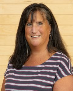 Head shot of Sheri Landry. Sheri is a white woman with long brown hair. She wearing a grey and white striped shirt and is smiling. 