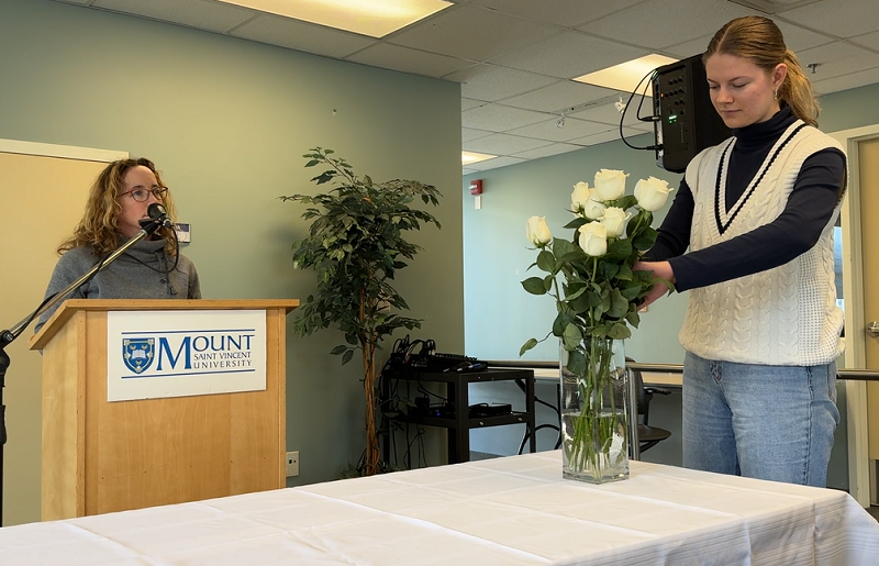 Dr. Isabelle Nault, speaking the names of the women who were killed at École Polytechnique, while a student places a white rose into a vase