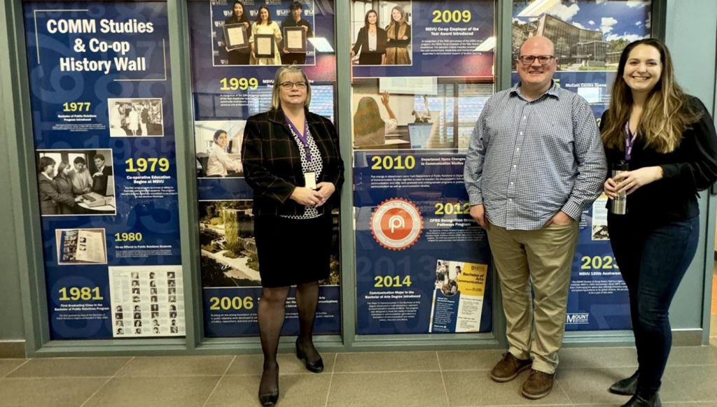 3 faculty and staff members from Communication Studies and Co-op standing in front of the new COMM Studies & Co-op History Wall