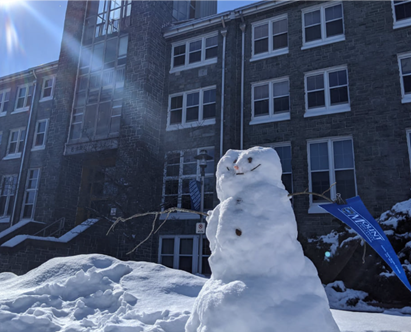 A snowman standing outside of Evaristus hall, holding a MSVU pennant