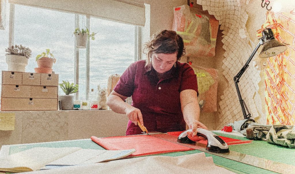 Melanie Colosimo, in a red shirt, measuring and cutting fabric