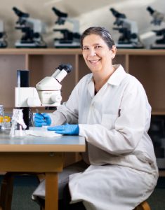 Dr. Tamara Franz-Odendaal sitting down beside a microscope doing lab work