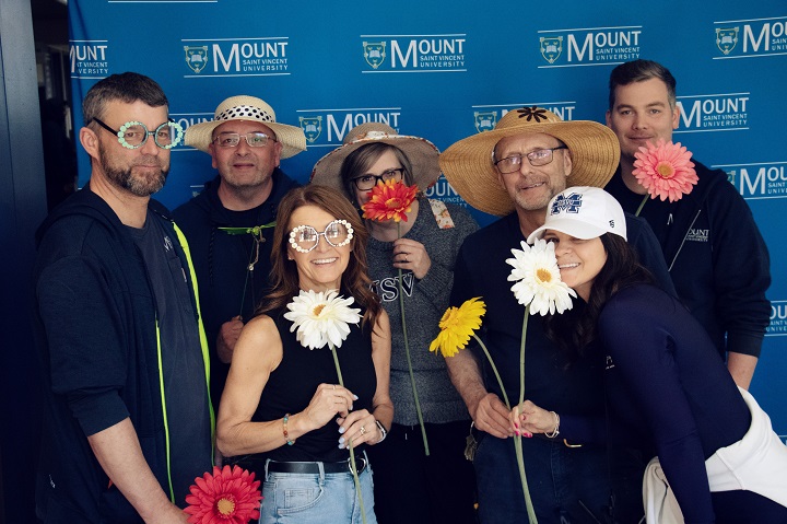 Several staff members posing at a photo booth with flowers and props