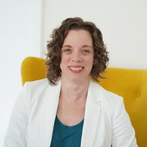 Natalie Lawy, sitting in a yellow chair smiling for the camera