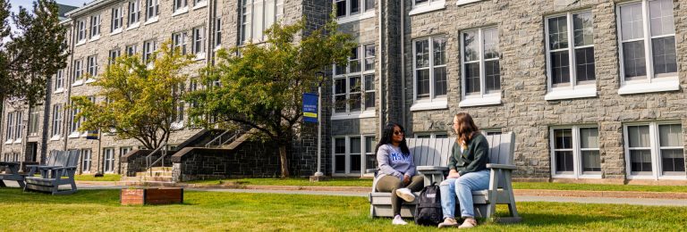 2 students sitting on a bench outside of Evaristus Hall