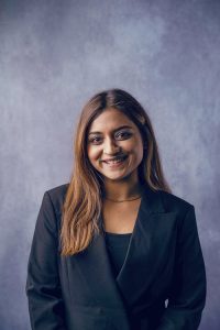 Simranpreet Kaur in a black blazer smiling at the camera