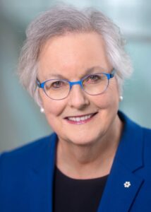 Dr. Anne Martin-Matthew, wearing a blue blazer and blue-framed glasses