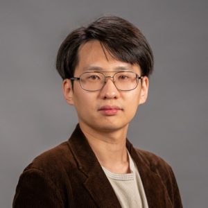 Zixian Liu, wearing a brown blazer and silver rimmed glasses