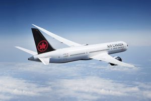 Air Canada Airplane flying in the blue sky with with clouds below. 