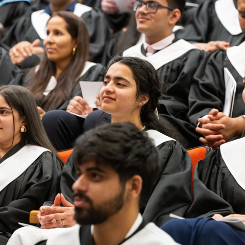 Students sitting in the auditorium during the Convocation ceremonies. The students are wearing the convocation gowns and listening to the address.
