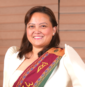 Dr. Dazzelyn Zapata, along a wooden panel backdrop and smiling at the camera