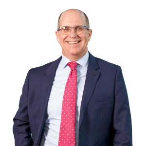 Patrick Sullivan, MSVU Business and Tourism CEO panelist, 2025. Patrick is a white man. He has a dark suit with a white buttoned shirt and a red tie. He is smiling and is standing against a white background. 