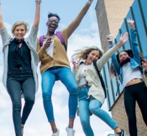 Four students jumping in excitement with their arms up and smiles on their faces. 