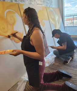 Two of the artists involved in the Two-Eyed Seeing Mural, painting on 3 large canvases