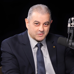 Chérif Matta, speaking into a microphone wearing a navy suit and tie