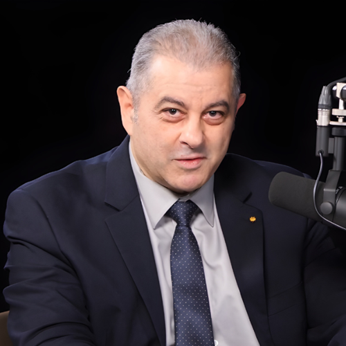 Chérif Matta, speaking into a microphone wearing a navy suit and tie
