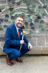Shane Donovan, in a blue suit, crouched down near Tanja Harrison's Women's Wall of Honour leaf