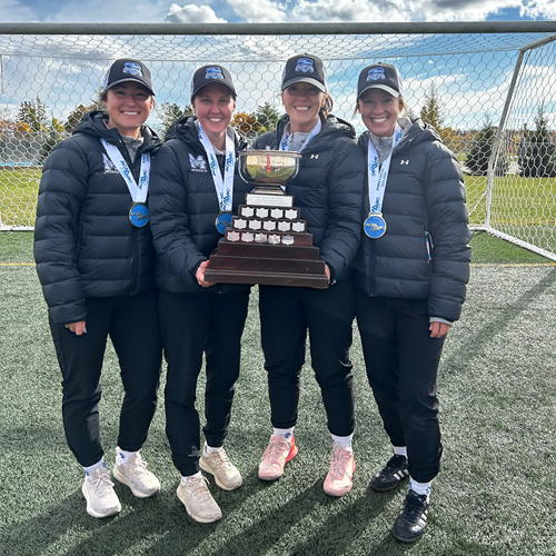 The 4 female coaches for the MSVU Women's soccer team: Ashley Poirier, Jenna Blackburn, Abby MacLeod, and Lauren Windsor, holding the ACAA trophy