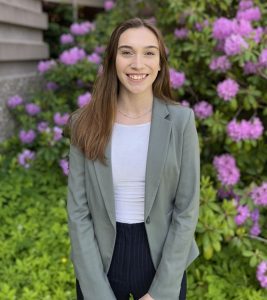 Laken Crowell, wearing an drab green blazer standing in front of some Hydrangeas