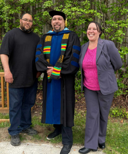 Martin Morrison, standing beside 2 family members posing for a photo in his PhD Convocation attire.