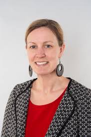 Dr. Catherine Baillie Abidi, wearing a patterned jacket and a red blouse, smiling at the camera