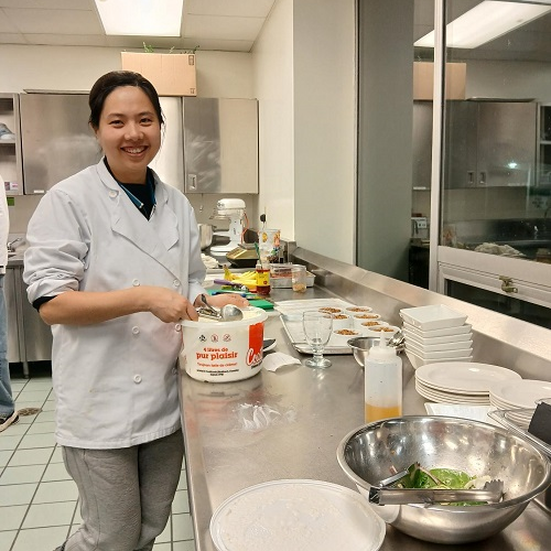 A Tourism and Hospitality student working in Vincent's Kitchen on campus, wearing a chef's attire and preparing a salad