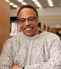 George Elliott Clarke, wearing a turtleneck sweater and grinning at the camera with his eyes closed