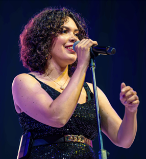 Julia Tynes singing into a microphone on stage wearing a black dress