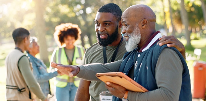 Two adults talking to each other. One has his hand on the other should, while the other points to the left. They are both wearing volunteer lanyards
