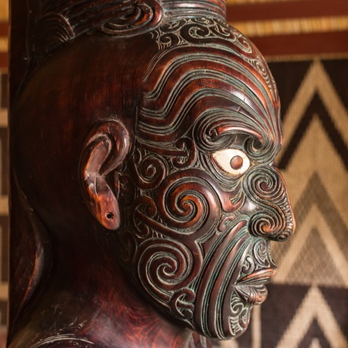 A Māori wood carving against a wooden wall