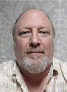 Dr. Michael Bowen, against a grey floral wallpaper wearing a white and olive plaid shirt
