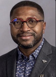 Orinari Wokoma, wearing a black blazer jacket and red rimmed glasses