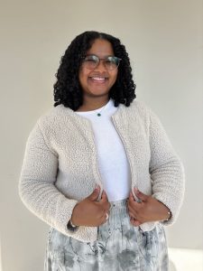 Suwela Paim Vaz Vassoa, wearing a cream cardigan and a white short, smiling at the camera