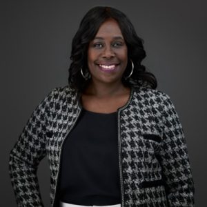 Wyndolyn Brown, wearing a houndstooth jacket and a black shirt against a black backdrop