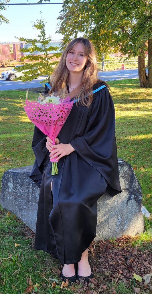 Sydney Davidson, dressed in a graduation gown, holding a bouquet of flowers