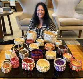 Cynthia Googoo, sitting down besides several woven baskets on a table.