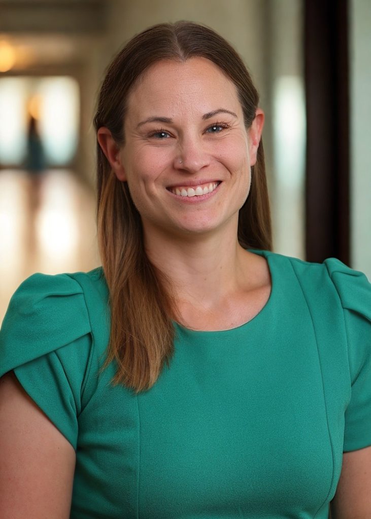 Dr. Justine Dol, wearing a turquoise shirt and has long brown hair, smiling at the camera