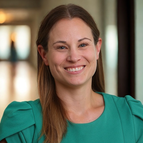 Dr. Justine Dol, wearing a turquoise shirt and has long brown hair, smiling at the camera