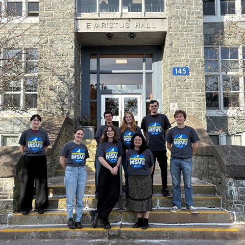 Several students standing outside Evaristus Hall posing for a group photo, wearing MSVU-branded tshirts.