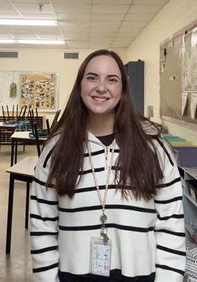 Sarah Monette, standing in a classroom and smiling at the camera