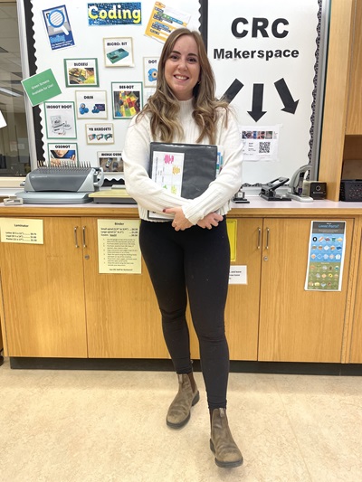 Sarah Monette, standing at the Curriculum Resource Centre and holding Education Textbooks